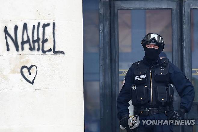 경찰 총에 사망한 나엘 군의 이름이 적힌 벽 옆에 선 경찰관 [AFP=연합뉴스. 재판매 및 DB 금지]