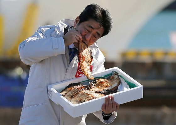 지난 2014년 12월 당시 아베 신조 일본 총리가 후쿠시마 지역의 한 항구에서 이 지역 생선구이를 직접 먹는 퍼포먼스를 하고 있다. 로이터=연합뉴스