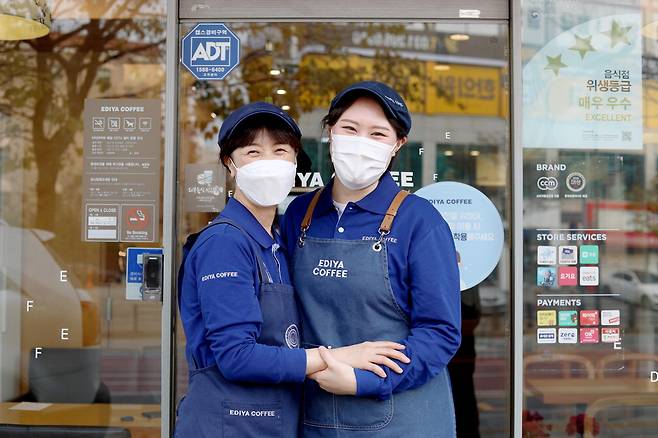 전국 매장에서 근무하는 아르바이트생(메이트)을 지원하는 '이디야 메이트 희망기금' 수혜를 받은 수원망포점의 최효빈 메이트(오른쪽)와 점주가 매장 앞에서 함께 웃고 있다.  이디야커피