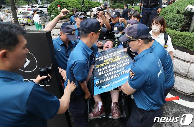 전국장애인차별철폐연대(전장연)이 12일 서울 중구 롯데호텔 지하주차장 출구에서 한덕수 국무총리와의 면담을 요청하며 시위를 벌이자 경찰이 휠체어를 탄 한 전장연 회원을 통행로 밖으로 들어 옮기고 있다. 한 총리는 이날 같은 장소에서 열린 정보보호의 날 기념식에 참석했다. 2023.7.12/뉴스1 ⓒ News1 허경 기자