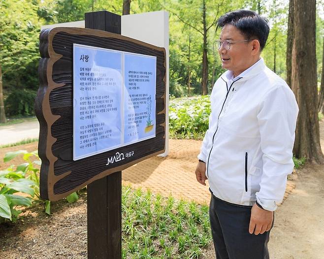 서울 마포구 박강수 구청장이 상암 하늘공원에 조성한 ‘시인의 거리’에 세워진 자신의 시 표지판(‘사랑’) 앞에서 웃고 있다. 지난 6월14일 촬영된 마포구 홍보사진