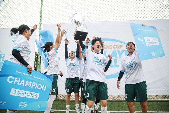 Members of the DIP FC futsal team lift the The Player: Futsal Queens Cup at the S-Build Futsal Park in Suwon, Gyeonggi on Sunday in a photo released by Puma on Wednesday. DIP FC emerged victorious in the inaugural 24-team competition sponsored by Puma and Musinsa to promote women's football in Korea.  [PUMA]