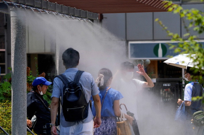 일본 도쿄에서 18일 보행자들이 더위를 식히기 위해 인공 물안개 밑을 걸어가고 있다. AFP 로이터 연합뉴스