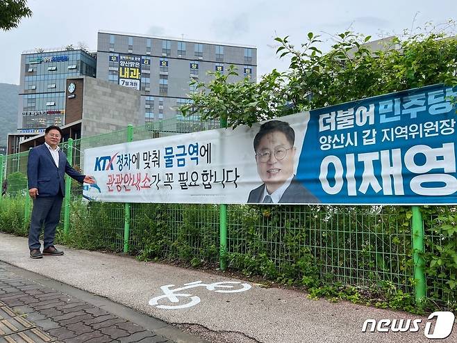 더불어민주당 이재영 양산갑위원장이 KTX 정차예정인 물금역 시 관광안내소 설치를 주장하는 플래카드 앞에 서 있다. (더불어민주당 양산갑지역위원회 제공)