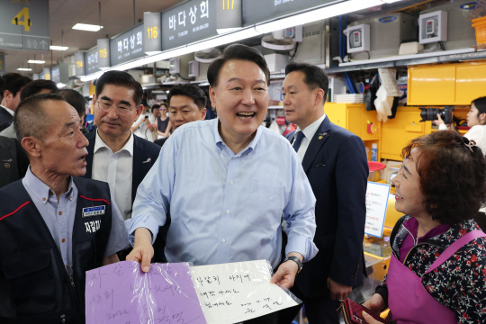 윤석열 대통령이 27일 부산 중구 자갈치시장에서 윤 대통령 본인의 사인을 모아온 한 상인과 인사하고 있다. 대통령실 제공