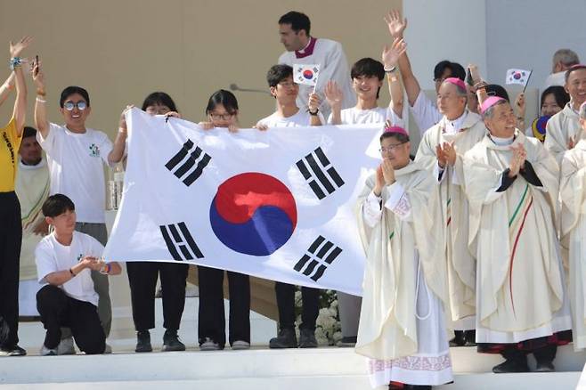 6일(현지시간) 포르투갈 리스본의 테주 공원에서 열린 올해 세계청년대회 폐막 미사에서 프란치스코 교황이 2027년 차기 대회 개최지를 서울로 발표되자 한국의 순례자들과 주교들이 무대 위에서 태극기를 펼쳐 들며 환호하고 있다. [이미지출처=AFP연합뉴스]