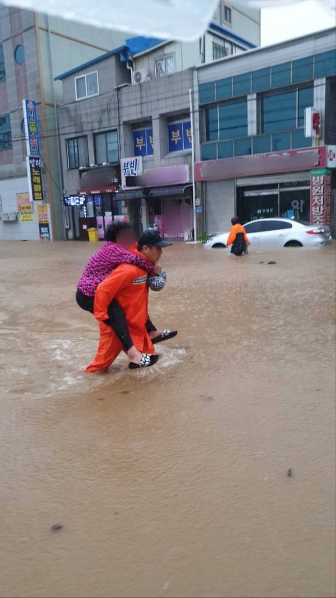 8.10.(목) 오후, 강원 고성군 거진읍에서 불어난 물로 도로가 침수되어 고립된 할머니를 출동한 소방대원이 업고 구조하고 있다.