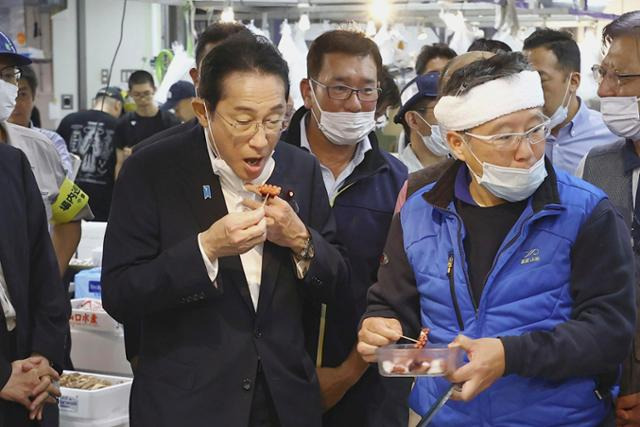 기시다 후미오(왼쪽) 일본 총리가 지난달 31일 일본 도쿄 도요스 수산시장을 찾아 해산물을 맛보고 있다. 도쿄=AP 뉴시스