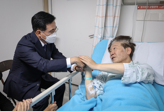 Democratic Party leader Lee Jae-myung, right, talks to Jin Gyo-hoon, chief of the Gangseo District, from his hospital bed on Friday. [DEMOCRATIC PARTY]