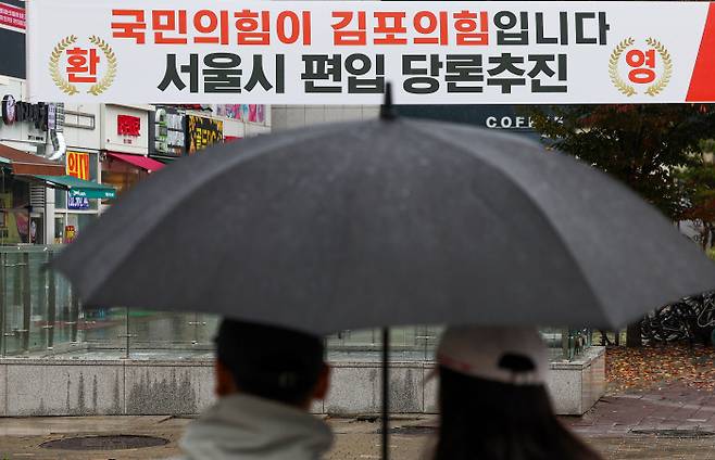 환영하는 여당 현수막  5일 오전 경기 김포시의 한 거리에서 주민들이 우산을 쓴 채 ‘김포의 서울시 편입 당론 추진’을 환영한다는 국민의힘 현수막을 지켜보고 있다. 연합뉴스