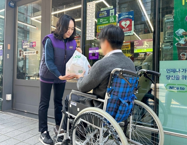 휠체어를 탄 장애인이 CU편의점 앞에서 픽업 서비스를 통해 사전 주문한 상품을 점원에게 받고 있다. BGF리테일은 휠체어 이용 장애인 등 이동약자를 위한 픽업 서비스를 도입한다고 밝혔다. BGF리테일 제공