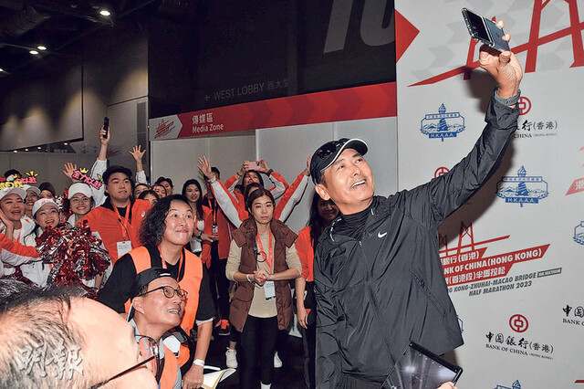 지난 19일(현지시각) 홍콩에서 열린 제1회 홍콩 주하이-마카오 대교 하프 마라톤 대회에 참가한 저우룬파(주윤발·가운데)가 대회 조직위원회 측 스태프들과 기념 사진을 촬영하고 있는 모습. 소후닷컴 누리집 갈무리
