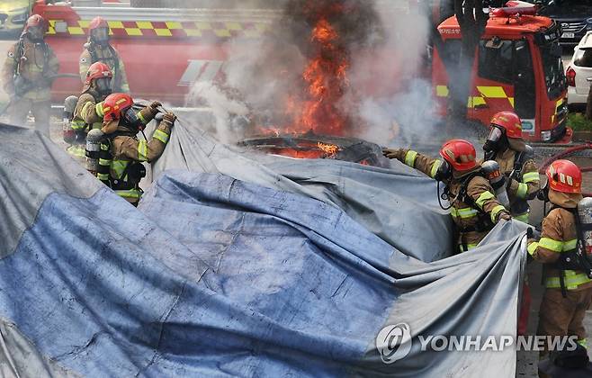 쉽게 꺼지지 않는 전기차 화재    지난 7월 21일 오후 경기도 용인시 경기도소방학교에서 열린 '전기자동차 실화재 진압 시연회'에서 소방관들이 질식소화덮개를 활용해 진화작업을 하고 있다. [연합뉴스 자료사진]