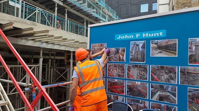 공사장 중간에 설치돼있는 파란 게시판에 붙어 있는 사진을 보고 토론 중인 현지 직원들. /백윤미 기자