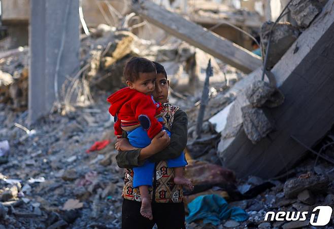 한 팔레스타인 소년이 4일(현지시간) 가자지구 라파 지역에서 아이를 들고 걱정스러운 눈빛으로 무너진 건물들을 바라보고 있다. 2023.12.04 ⓒ 로이터=뉴스1 ⓒ News1 정지윤 기자