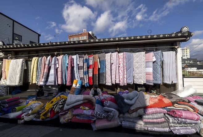 다가오는 겨울을 위해 이불을 가지고 나온 장꾼이 처마 밑에 형형색색 이불을 걸어놓았다.