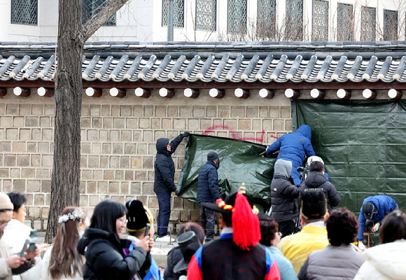 문화재청 궁능유적본부 직원들이 지난 16일 오전 서울 종로구 국립고궁박물관 방향 경복궁 서편에서 스프레이 낙서로 훼손된 담벼락을 천으로 덮고 있다. [사진=뉴시스]