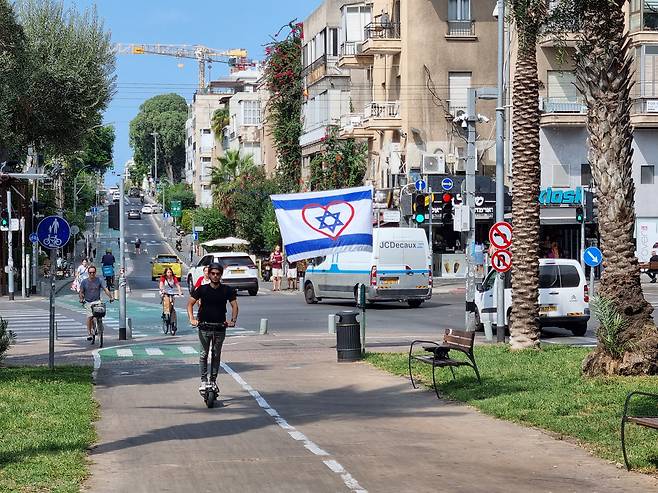 9일(현지 시각) 이스라엘 텔아비브 시내 미호엘스 광장에서 가자지구 무장 정파 하마스의 공습으로 숨진 사망자와 부상자를 추모하고 이스라엘 군인들을 지지하는 의미로 시민들이 내건 깃발이 걸려있다. 깃발은 이스라엘 국기에 붉은 색 하트를 그렸다. /텔아비브=정철환 특파원
