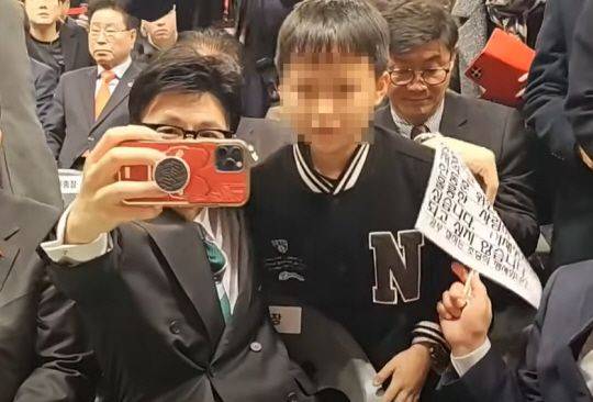 지난 4일 충북 청주시 장애인스포츠센터에서 열린 국민의힘 충북도당 신년 인사회에서 한동훈 국민의힘 비상대책위원장이 한 어린이와 사진을 찍기 전 이 아이가 가져온 피켓을 어깨 너머로 치우고 있다. /사진=유튜브 '김사랑 시인' 캡처,문화일보