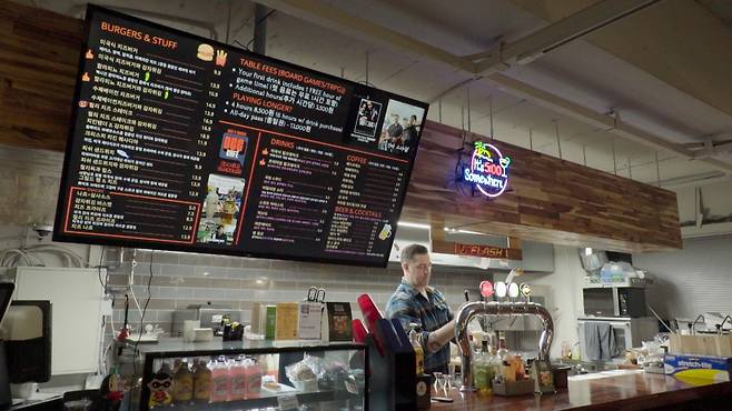 Joey Croner, owner of Dice and Comics Cafe, pours a beer behind the counter. (The Korea Herald)