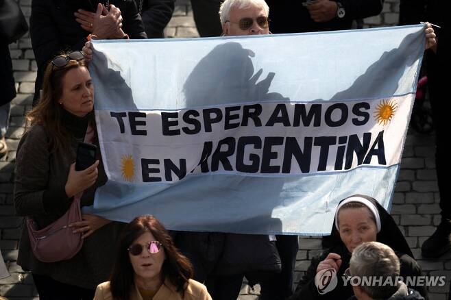 "아르헨티나는 당신을 기다리고 있습니다" (바티칸 로이터=연합뉴스) 프란치스코 교황이 14일(현지시간) 바티칸 성 베드로 광장에서 주일 삼종기도를 주례한 가운데 한 남성이 아르헨티나 국기 색깔의 천을 들고 있다. 여기에는 "아르헨티나는 당신(프란치스코 교황)을 기다리고 있다"는 글귀가 적혔다. 2024.01.14 photo@yna.co.kr