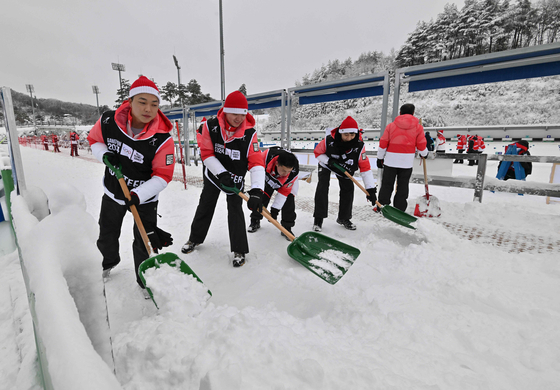 Volunteers clear snow ahead of the single mixed relay biathlon during the Gangwon 2024 Winter Youth Olympic Games at Alpensia Biathlon Centre in Pyeongchang on Sunday. [AFP/YONHAP]