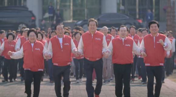 위 사진은 새누리당 측인 2016년  공천장에 도장을 찍지 못하겠다며 부산으로 간 김 전 대표와 이를 쫓아간 원유철 전 원내대표를 희화화한 일종의 홍보 영상 일부. 영상 마지막에 다른 최고위원들까지 모두 다 같이 손을 잡고 뛰며 당시 새누리당 내 친박(친 이명박계)과 비박 사이 공천 갈등을 봉합했다는 취지를 담아냈다.  [사진=유튜브 '국민의힘TV' 캡처]