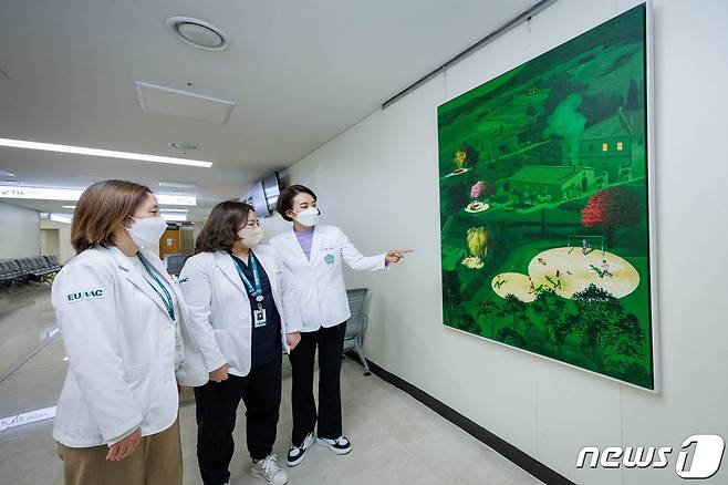 이화의료원 관계자들이(사진 좌측부터 대외협력부 김미경 실장, 김소정 부실장, 전혜진 부장) 이대목동병원 1층에 전시된 드림그림 기증 작품을 살펴보고 있다. (사진제공=한성자동차)