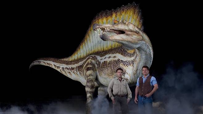 2014년 사이언스지에 아프리카에서 발굴한 스피노사우루스 화석을 발표한 폴 세레노 교수(오른쪽)와 니자르 이브라힘 박사. 뒤로 등에 거대한 돛 모양 구조가 있는 스피노사우루스 상상도가 보인다. 두 사람은 이후 스피노사우루스가 물속에서 사냥했는지, 물가에서 물고기를 집어올렸는지를 두고 의견이 갈렸다./미 시카고대