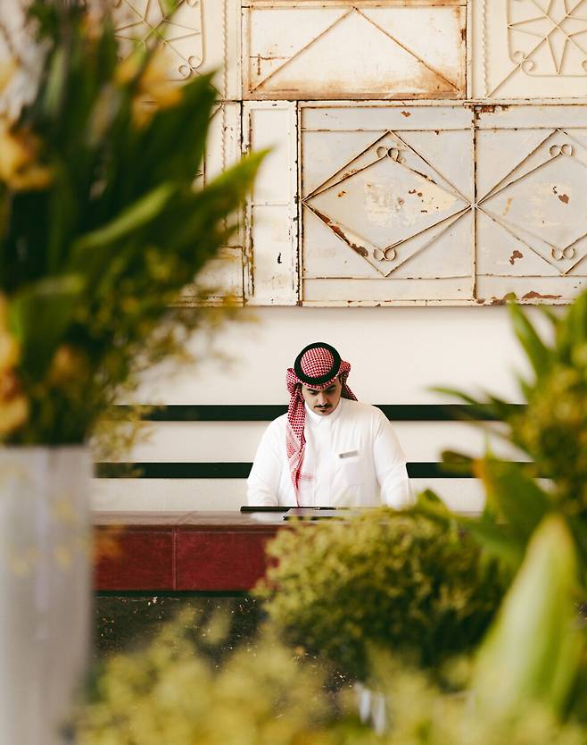 리셉션에서 여행자를 맞이하는 직원. 하얀색 전통 복장인 싸웁(Thawb)과 붉은색 체크무늬 천 쉬마그(Shmag)를 두르고 있다. 그를 보고 사우디아라비아에 왔음을 실감한다