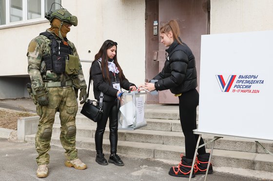 11일 러시아에 점령 당한 우크라이나 도네츠크에서 한 여성이 군인이 지켜보는 가운데 투명 투표함에 투표용지를 넣고 있다. 타스=연합뉴스