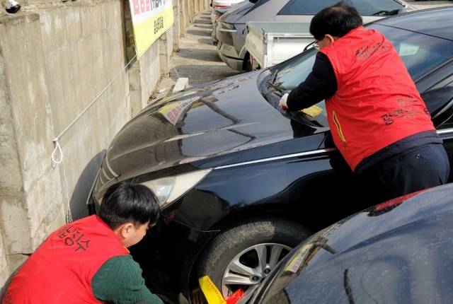 ▲경남 창녕군 체납 차량 번호판 영치기동반이 벽면에 밀착 주차한 체납차량에 바퀴 잠금장치 설치하고 있다.ⓒ창녕군