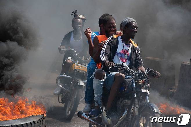 아이티의 수도 포르토프랭스의 거리에서 타이어들이 불에 타며 연기를 내뿜고 있는 가운데 한 무리의 남성들이 오토바이를 타고 질주하고 있다. 2024.03.12 ⓒ AFP=뉴스1 ⓒ News1 정지윤 기자