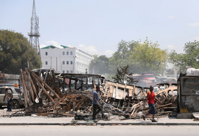 3월 25일 아이티 수도 포르토프랭스의 대통령궁 근처에서 불에 탄 차량 잔해를 사람들이 지나치고 있다. 로이터연합뉴스