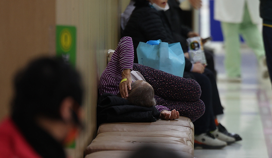 An elderly patient lies on a bench as she waits to see a doctor at a university hospital in Daegu on Friday. [YONHAP]