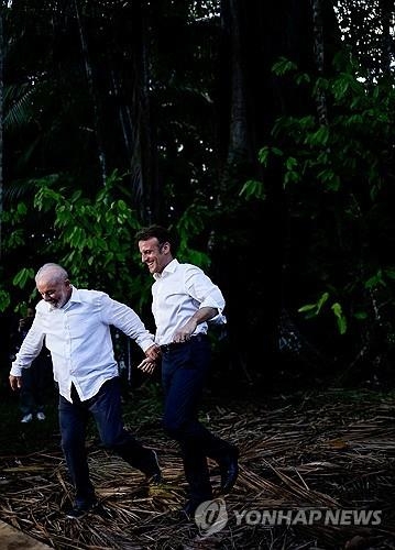 콤부 섬에서 손 잡고 달려가는 룰라 대통령(왼쪽)과 마크롱 대통령의 모습.[사진 = 로이터 연합뉴스]