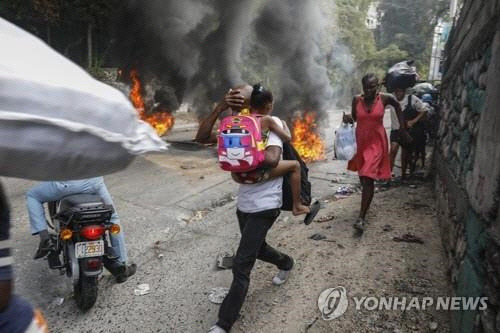 지난 2월 5일(현지시간) 아이티 수도 포르토프랭스에서 행인들이 불붙은 폐타이어 옆을 황급히 지나가고 있다. 아리엘 앙리 총리 사임을 요구하는 시위대는 도로를 점거한 채 폐타이어에 불을 지르거나 주요 시설물에 돌을 던지면서 격렬한 시위를 벌였다. (포르토프랭스 AP=연합뉴스)