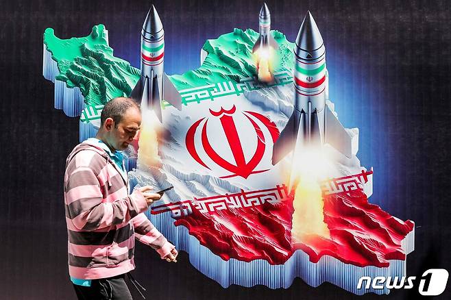 15일(현지시간) 이란 테헤란의 한 거리에 걸려 있는 이란 국기와 미사일 벽화 앞으로 한 남성이 휴대폰을 하며 걸어가고 있다. 2024.04.15 ⓒ AFP=뉴스1 ⓒ News1 정지윤 기자