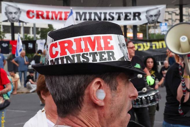 한 이스라엘 시민이 지난 27일(현지시간) 이스라엘 텔아비브에서 열린 반정부 시위에서 베냐민 네타냐후 총리를 ‘범죄자’라고 칭한 구호가 적힌 모자를 쓰고 있다. AFP연합뉴스