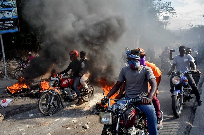 아이티 수도 포르토프랭스에서 오토바이를 탄 시위대가 화염과 시커먼 연기로 뒤덮인 거리를 지나가고 있다. [연합]
