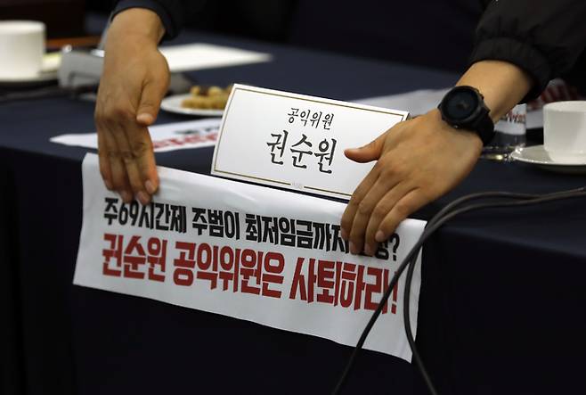 4월 18일 서울 프레스센터에서 최저임금위원회 제1차 전원회의를 앞두고 양대노총 관계자들이 권순원 공익위원 자리에 피켓을 붙이고 있다. 뉴시스