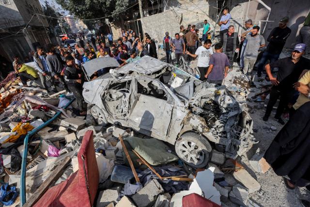 팔레스타인 주민들이 14일 가자지구 중부 알누세이라트 난민촌에 가해진 이스라엘군의 공습으로 파괴된 차량 잔해 주위에 모여 있다. 알누세이라트=로이터 연합뉴스