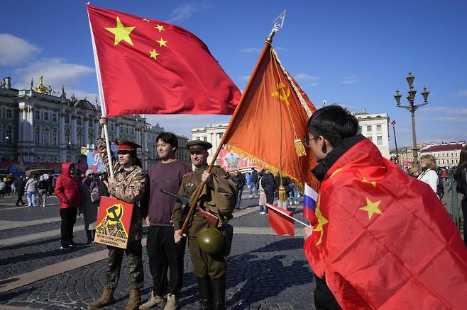 지난 9일(현지시간) 제 2차 세계대전 전승 기념일을 맞은 러시아 상트페테르부르크에서 중국 유학생들이 옛 소련 복장을 입고 소련 깃발을 든 러시아 역사 동호회 회원(왼쪽 세번째)과 사진을 찍고 있다.AP뉴시스