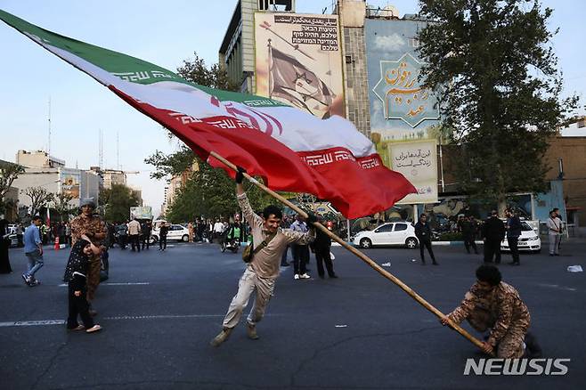 [테헤란=AP/뉴시스] 지난달 15일(현지시각) 이란 테헤란에서 반이스라엘 메시지가 그려진 한 건물 앞에서 시위대가 커다란 이란 국기를 흔드는 모습. 2024.05.20.