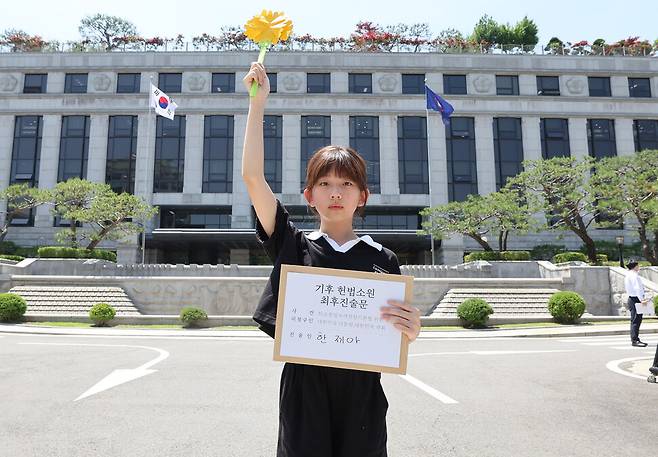 한국 정부의 기후 변화 대응이 헌법에 합치하는지를 묻는 기후소송 두 번째 공개 변론이 열린 21일 오후 서울 종로구 헌법재판소 앞에서 최종 진술자 3인 중 한 명인 한제아 아기기후소송 청구인이 최후 진술문과 ‘반드시 행복은 오고야 만다’는 꽃말의 메리골드 종이꽃을 손에 들고 있다. 백소아 기자 thanks@hani.co.kr