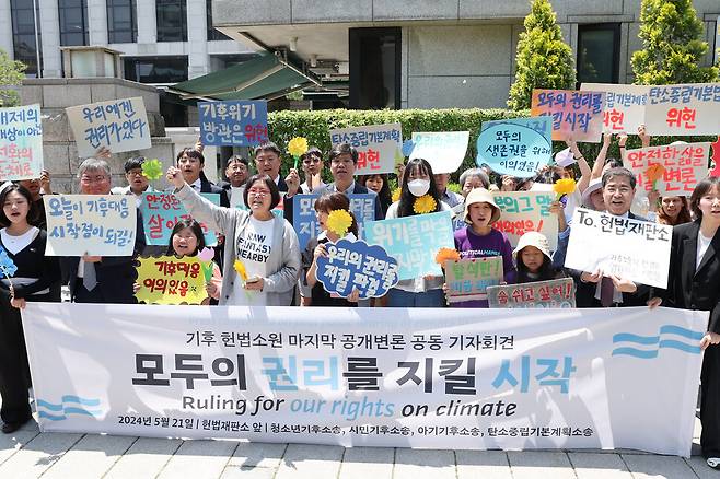 한국 정부의 기후 변화 대응이 헌법에 합치하는지를 묻는 기후위기 헌법소원 두 번째 공개 변론이 열린 21일 오후 서울 종로구 헌법재판소 앞에서 기후소송 원고 단체와 공동 대리인단이 기자회견을 열어 구호를 외치고 있다. 참가자들은 ‘반드시 행복은 오고야 만다’는 꽃말의 메리골드를 손수 접어들었다. 백소아 기자