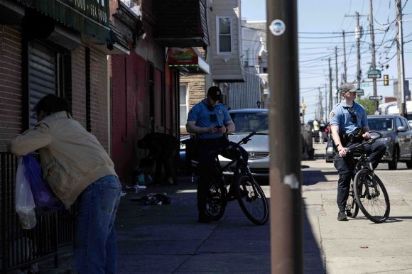 마약에 취한 여성 너머로 자전거를 탄 지역 경찰들이 거리에 멈춰있다.
