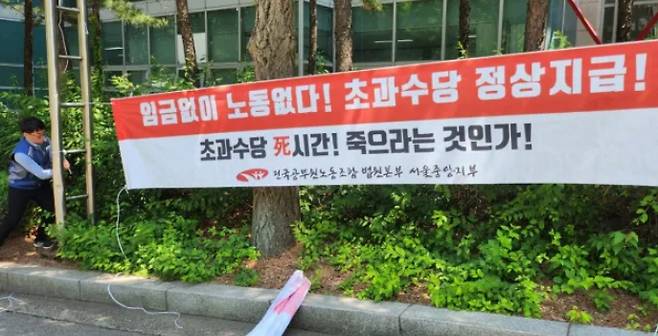 A member of the Seoul Central Branch of the National Public Employees\' Labor Union Court Headquarters hangs a banner demanding normal payment of overtime wages in front of the Seoul Central District Court in Seocho-gu, Seoul, on Nov. 21.