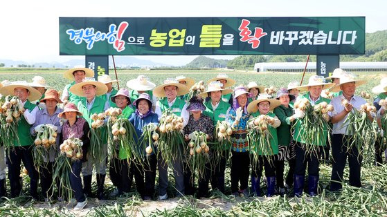 지난 23일 경북 문경시 영순면 공동영농단지에서 ‘경북 농업대전환 공동영농 성과 보고회’가 열린 가운데 참석자들이 농민들과 함께 수확한 양파를 들고 기념촬영하고 있다. [사진 경북도]