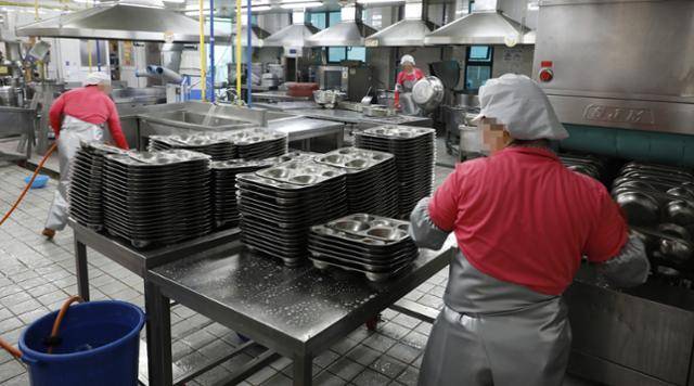 급식실 노동자를 비롯해 학교 비정규직 노동자들이 전국 총파업을 벌이기 전날인 2019년 7월 2일 한 초등학교 급식실에서 노동자들이 식판 등을 정리하고 있다. 사진에 보이는 것처럼 급식실 노동자들은 '위생 문제'를 이유로 위생복 상하의, 위생 장화, 고무장갑, 팔 토시, 마스크, 위생모 등 온몸을 꽁꽁 싸매고 일한다. 중무장 차림에 요리하며 발생하는 증기, 열기 등이 더해지면 체감온도는 50도에 가깝다고 한다. 한국일보 자료사진